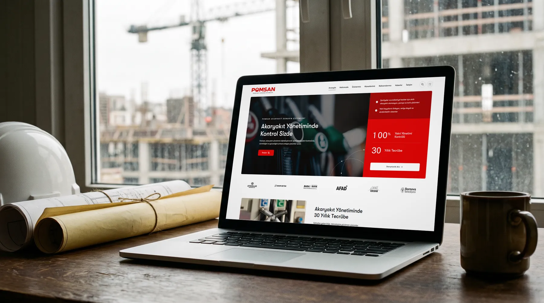 Şantiye ofisinde masada açık laptop, ekranda pomsan.com.tr anasayfası